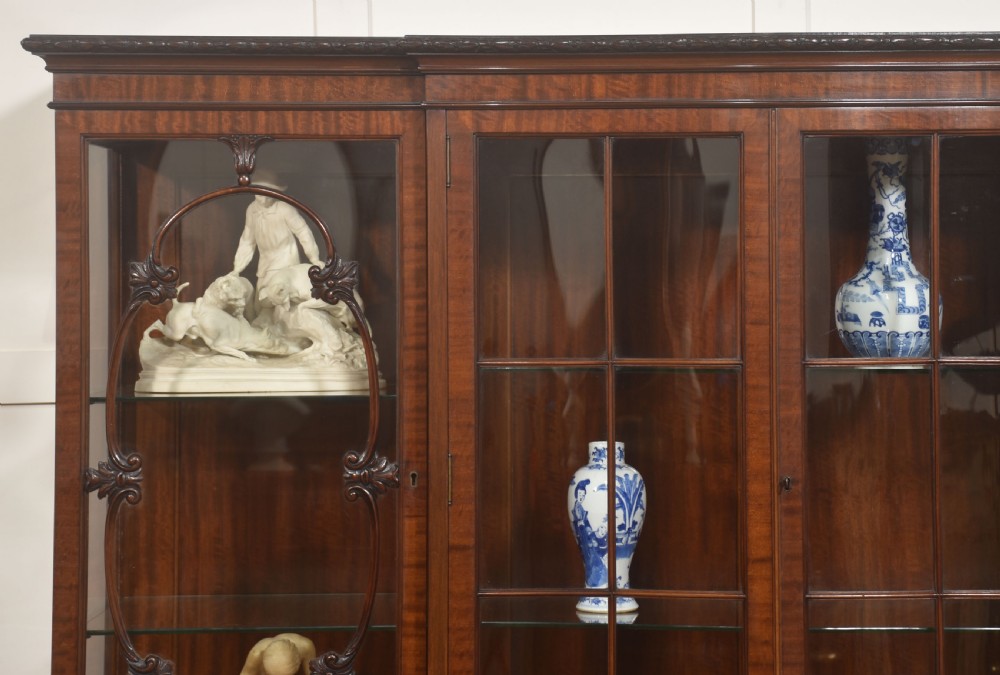 A Chippendale Revival breakfront display cabinet in carved mahogany featuring glazed doors, interior glass shelves, lower cupboards, and claw-and-ball feet. View II