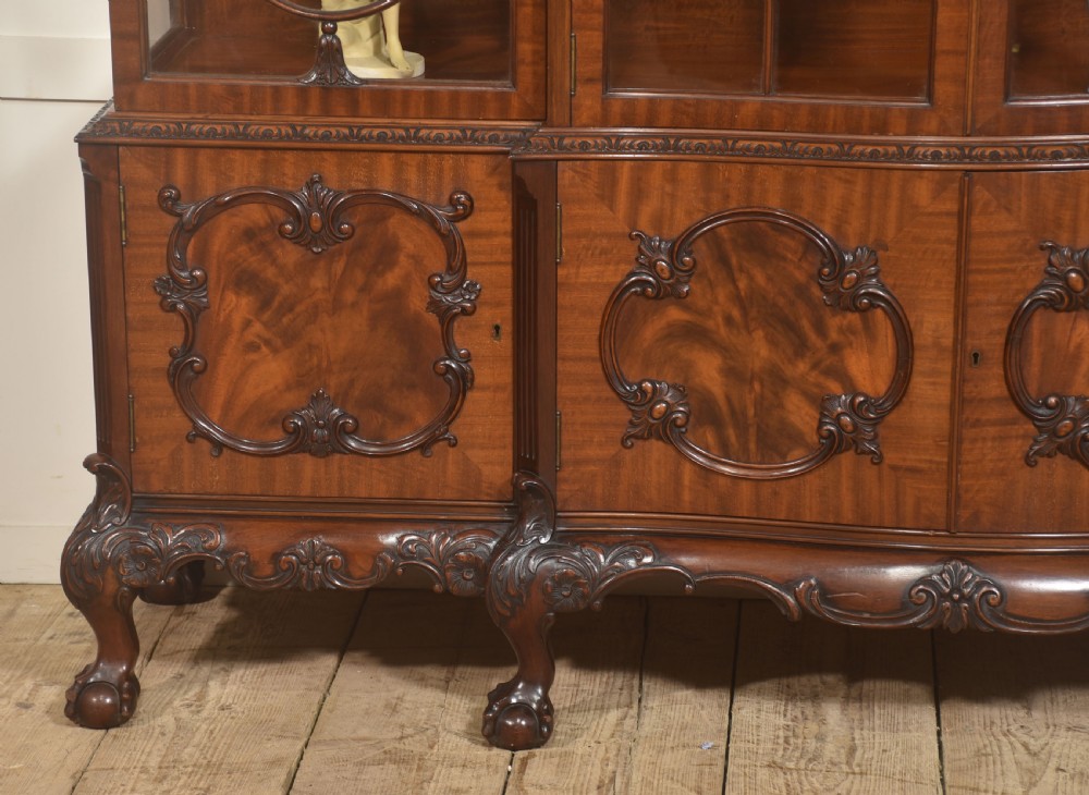 A Chippendale Revival breakfront display cabinet in carved mahogany featuring glazed doors, interior glass shelves, lower cupboards, and claw-and-ball feet. View III