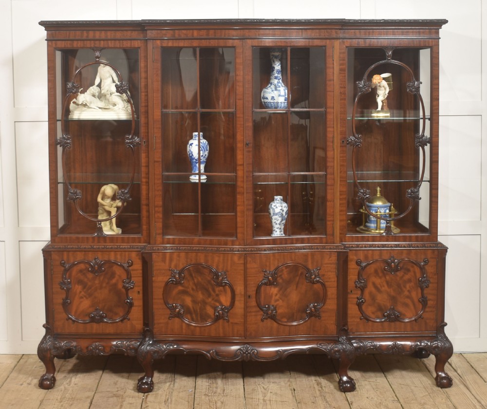 A Chippendale Revival breakfront display cabinet in carved mahogany featuring glazed doors, interior glass shelves, lower cupboards, and claw-and-ball feet. View IV
