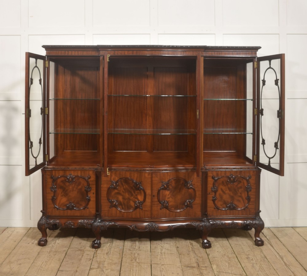 A Chippendale Revival breakfront display cabinet in carved mahogany featuring glazed doors, interior glass shelves, lower cupboards, and claw-and-ball feet. View VII