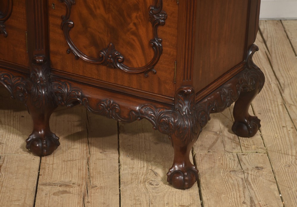 A Chippendale Revival breakfront display cabinet in carved mahogany featuring glazed doors, interior glass shelves, lower cupboards, and claw-and-ball feet. View XI
