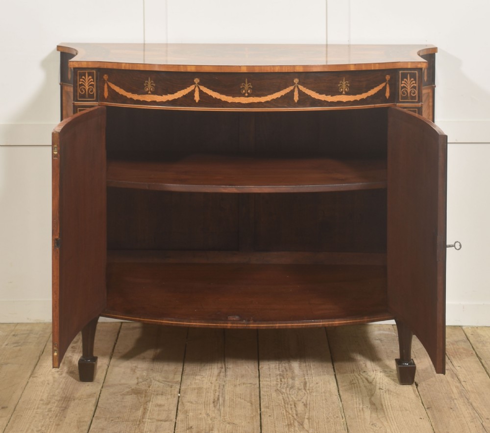 A George III style satinwood and rosewood marquetry sideboard featuring oval cabinet doors with inlaid urn medallions, floral swags, and tapered square legs. View III