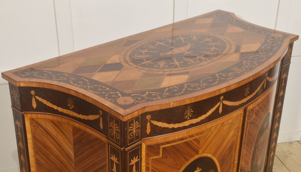 A George III style satinwood and rosewood marquetry sideboard featuring oval cabinet doors with inlaid urn medallions, floral swags, and tapered square legs. View V