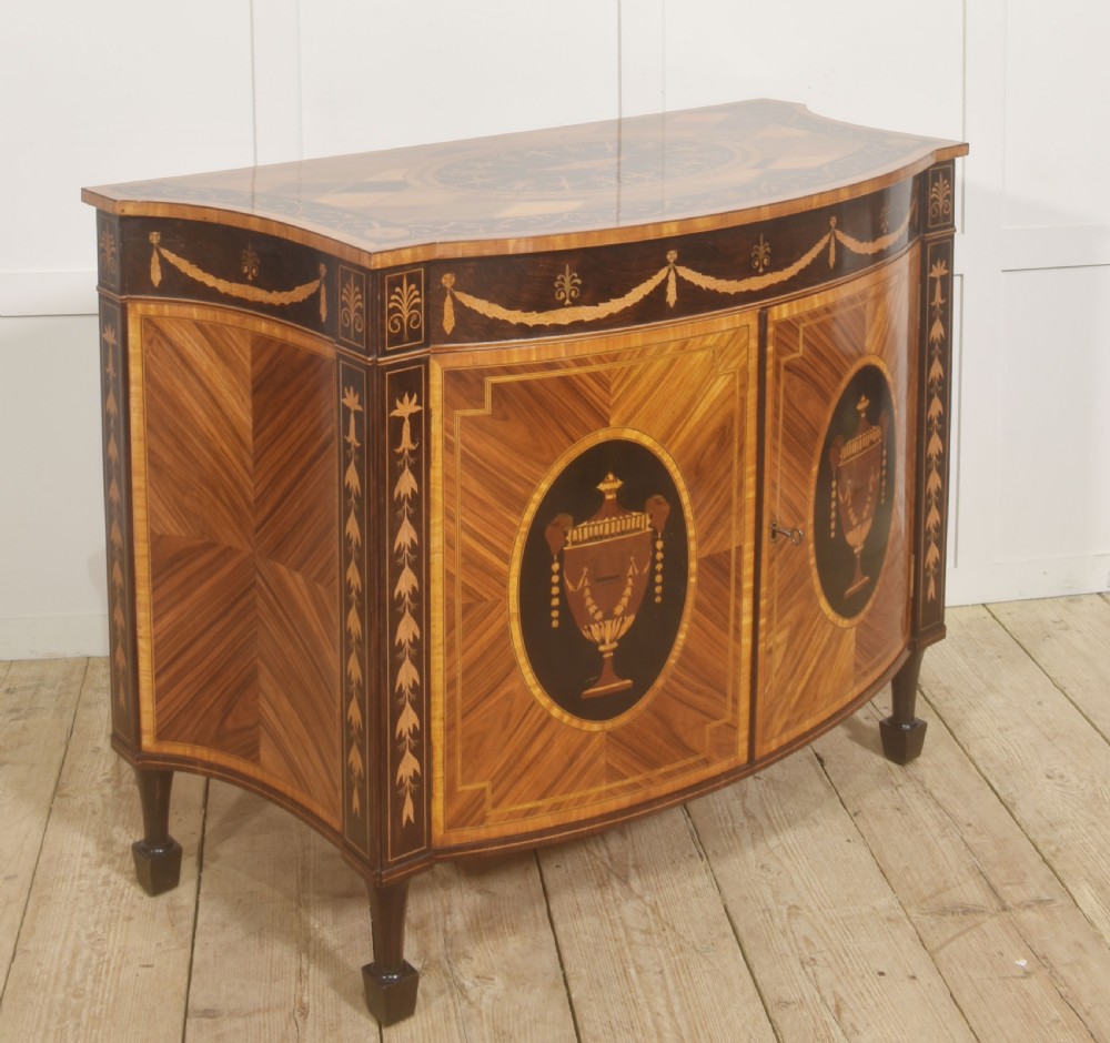 A George III style satinwood and rosewood marquetry sideboard featuring oval cabinet doors with inlaid urn medallions, floral swags, and tapered square legs. View VI