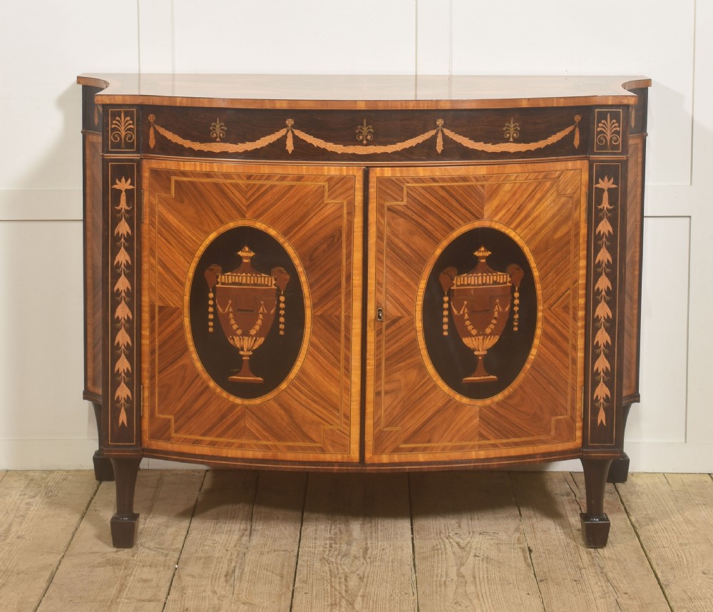 A George III style satinwood and rosewood marquetry sideboard featuring oval cabinet doors with inlaid urn medallions, floral swags, and tapered square legs. View XI