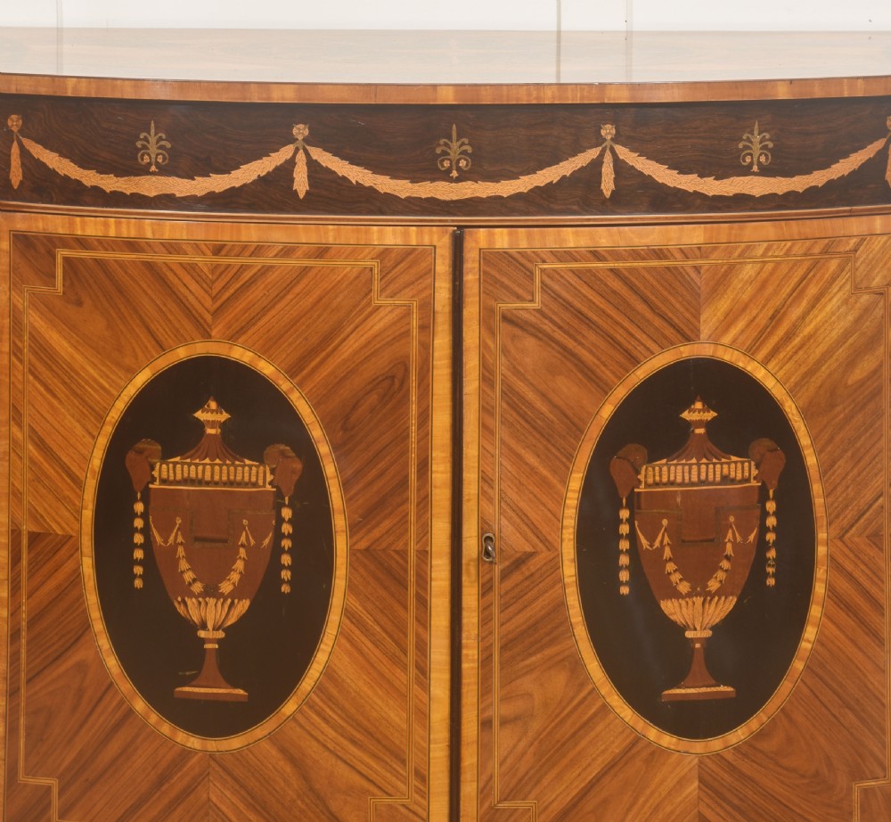 A George III style satinwood and rosewood marquetry sideboard featuring oval cabinet doors with inlaid urn medallions, floral swags, and tapered square legs. View XII