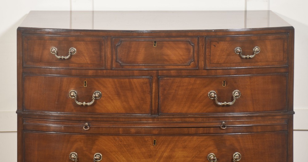 A tall George III style mahogany serpentine chest of drawers featuring flame mahogany grain and brass swan-neck handles. View II