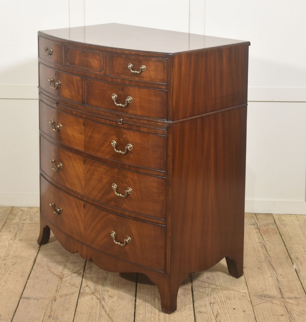 A tall George III style mahogany serpentine chest of drawers featuring flame mahogany grain and brass swan-neck handles. View IV
