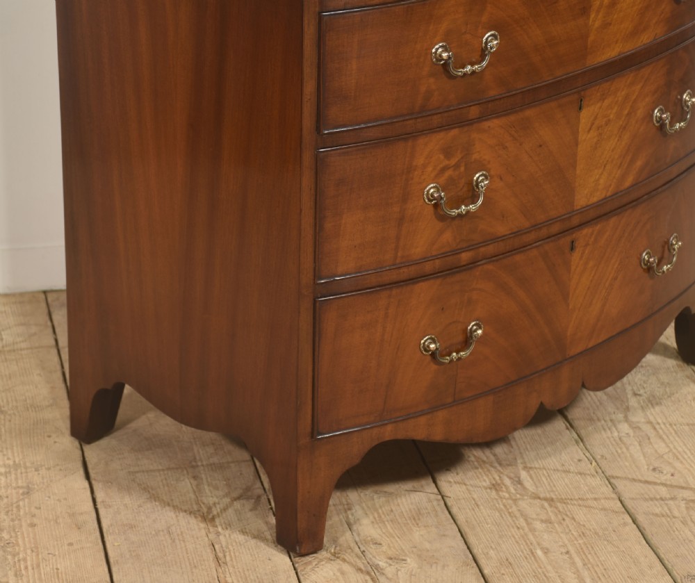 A tall George III style mahogany serpentine chest of drawers featuring flame mahogany grain and brass swan-neck handles. View VI