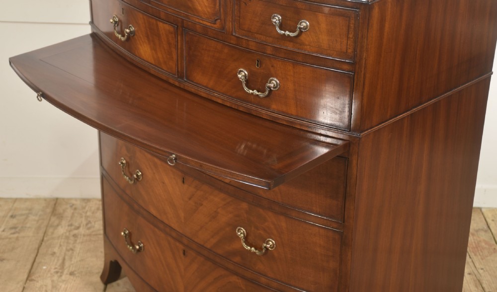 A tall George III style mahogany serpentine chest of drawers featuring flame mahogany grain and brass swan-neck handles. View VIII