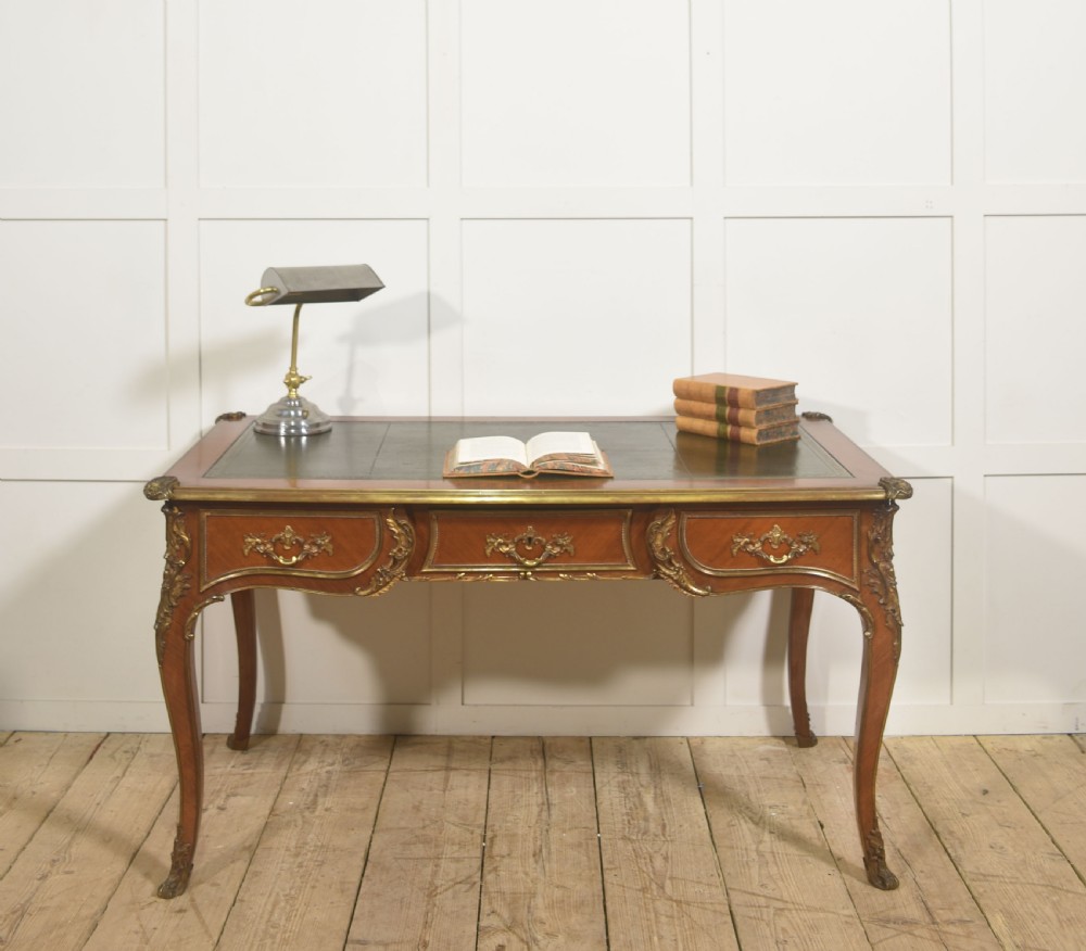 A French Louis XV style wooden bureau plat featuring three frieze drawers, gilt-bronze ormolu mounts, cabriole legs, and a green leather writing surface. View II