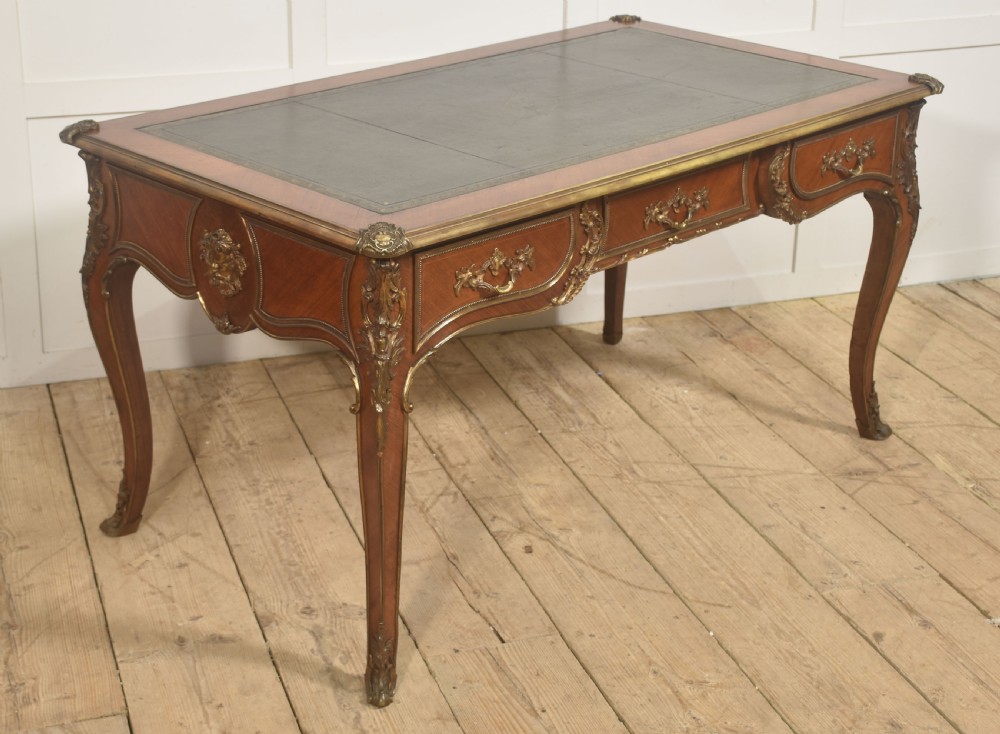 A French Louis XV style wooden bureau plat featuring three frieze drawers, gilt-bronze ormolu mounts, cabriole legs, and a green leather writing surface. View V