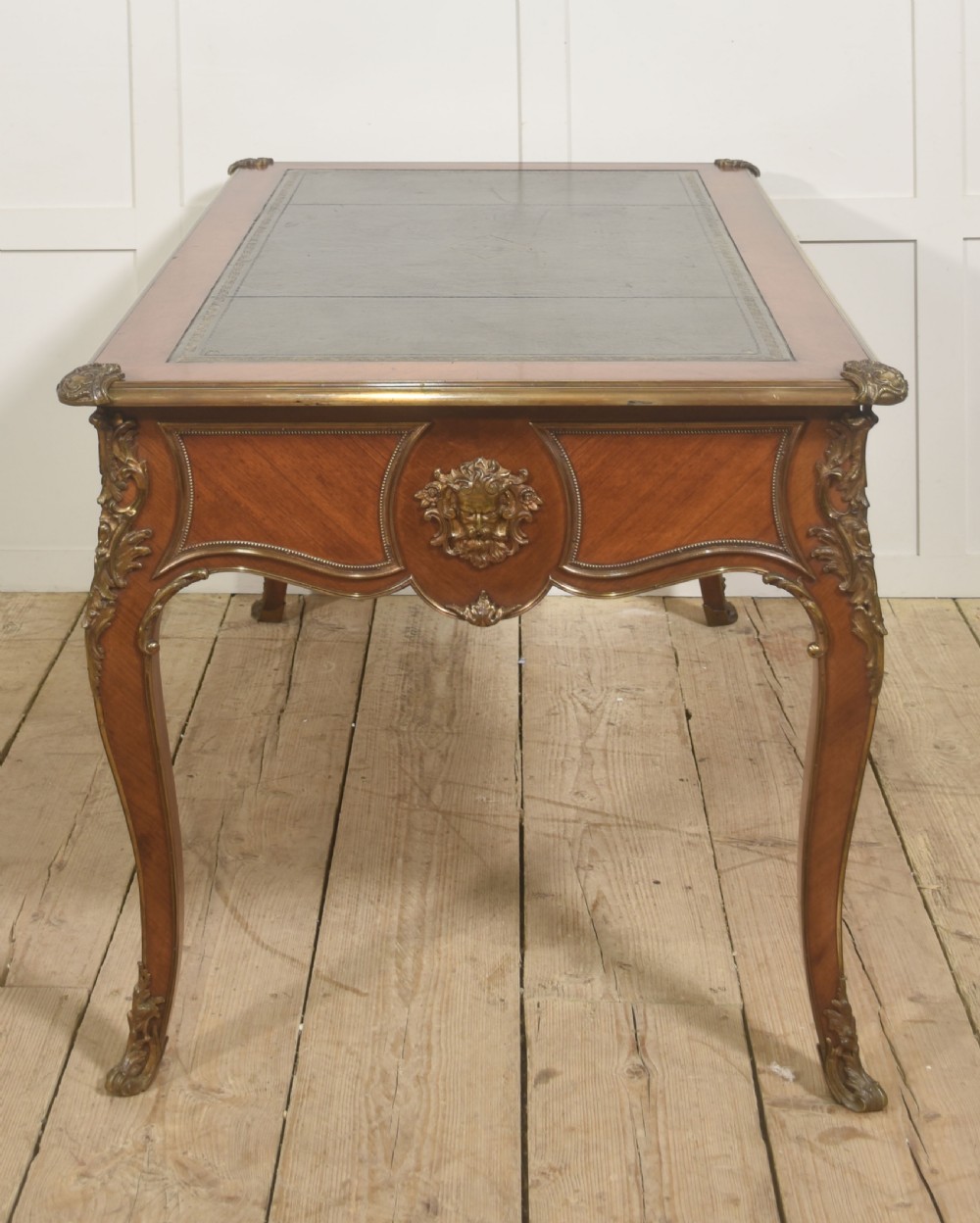 A French Louis XV style wooden bureau plat featuring three frieze drawers, gilt-bronze ormolu mounts, cabriole legs, and a green leather writing surface. View X