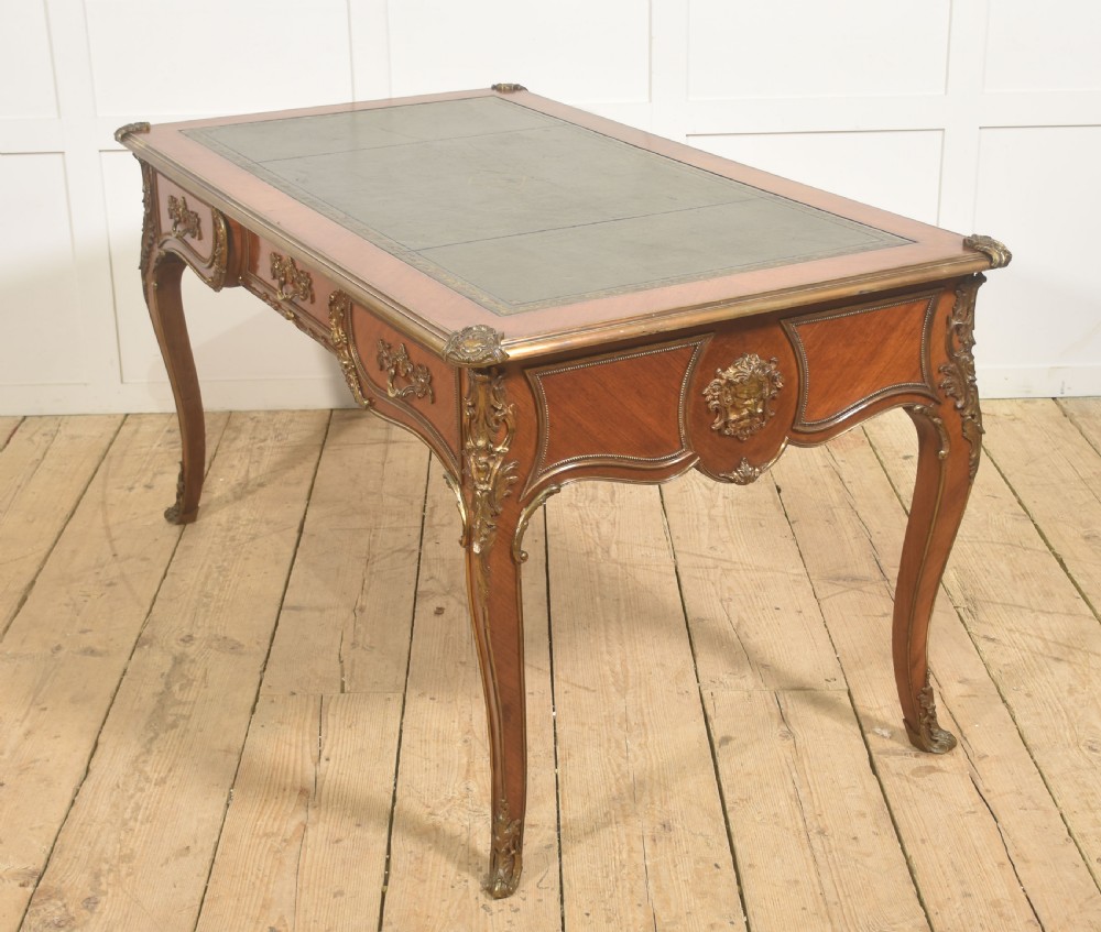 A French Louis XV style wooden bureau plat featuring three frieze drawers, gilt-bronze ormolu mounts, cabriole legs, and a green leather writing surface. View XII