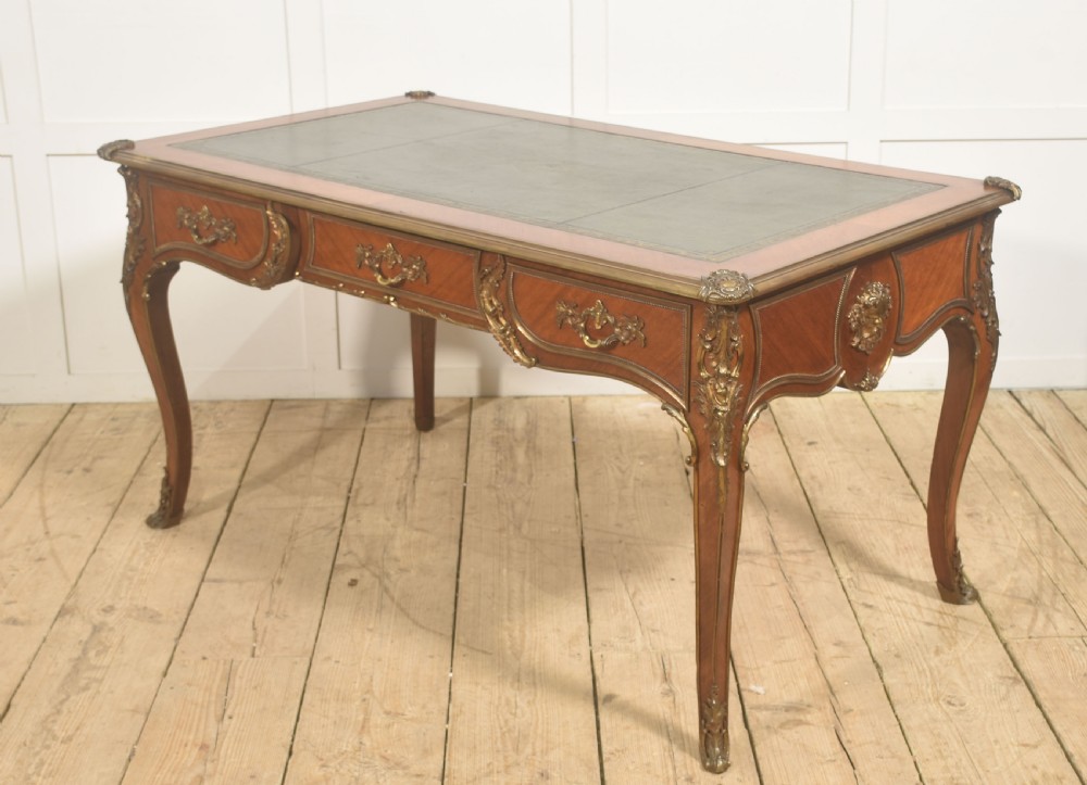 A French Louis XV style wooden bureau plat featuring three frieze drawers, gilt-bronze ormolu mounts, cabriole legs, and a green leather writing surface. View XIII