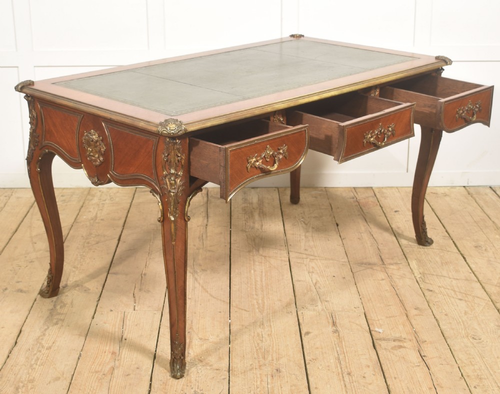 A French Louis XV style wooden bureau plat featuring three frieze drawers, gilt-bronze ormolu mounts, cabriole legs, and a green leather writing surface. View XIV