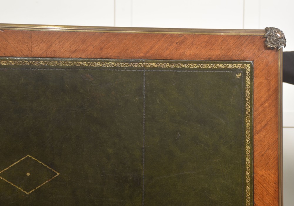 A French Louis XV style wooden bureau plat featuring three frieze drawers, gilt-bronze ormolu mounts, cabriole legs, and a green leather writing surface. View XVIII