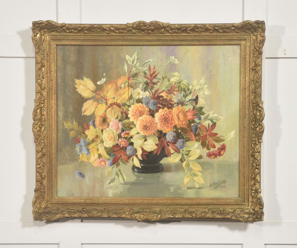 A framed oil painting on canvas depicting a still life arrangement of orange and yellow autumn flowers in a dark vase set within an ornate carved gilt frame.