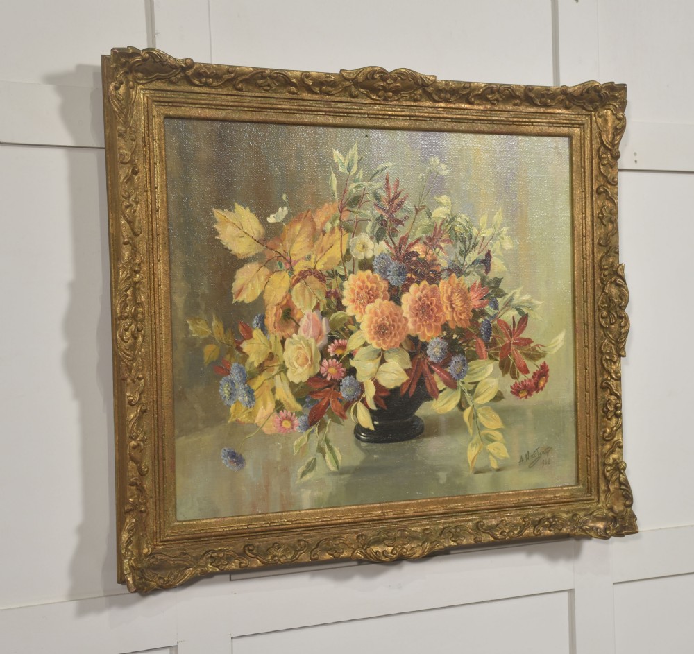 A framed oil painting on canvas depicting a still life arrangement of orange and yellow autumn flowers in a dark vase set within an ornate carved gilt frame. View V