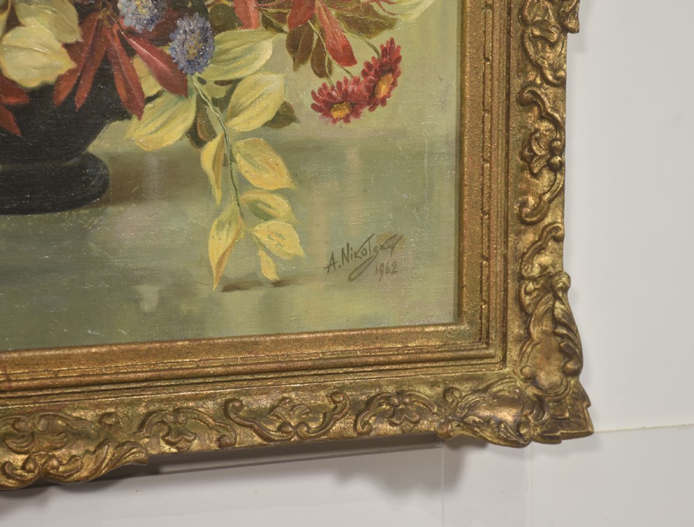 A framed oil painting on canvas depicting a still life arrangement of orange and yellow autumn flowers in a dark vase set within an ornate carved gilt frame. View VII