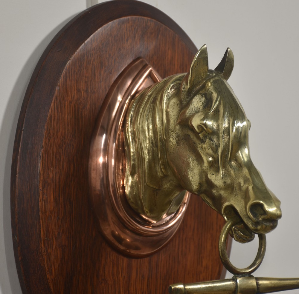 A wall-hanging oak oval plaque featuring a cast brass horse head mount supporting a circular brass dinner gong with a suspended striker. View IV