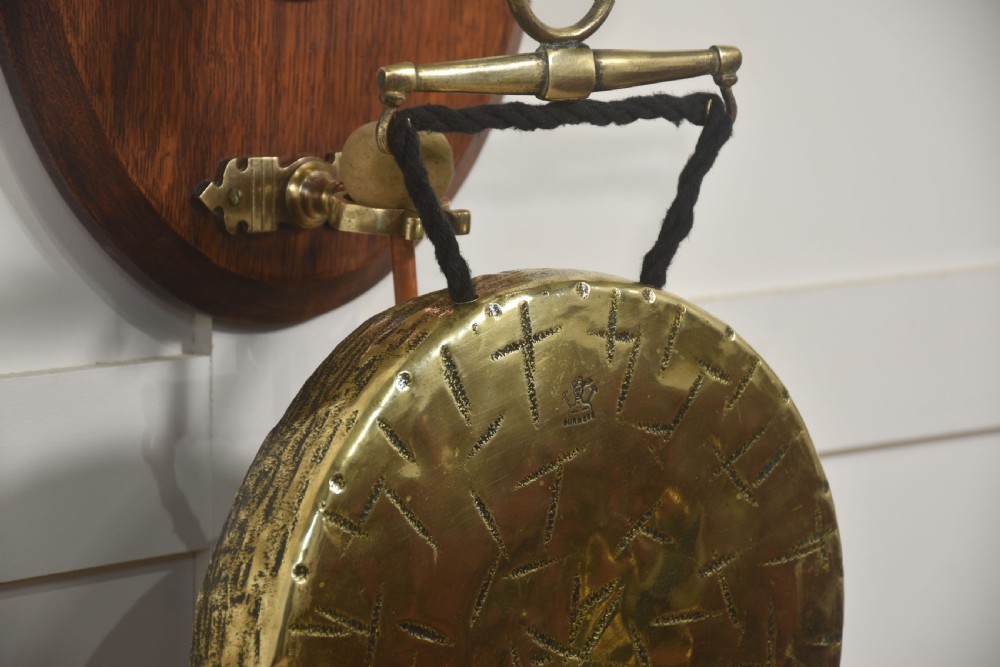 A wall-hanging oak oval plaque featuring a cast brass horse head mount supporting a circular brass dinner gong with a suspended striker. View V