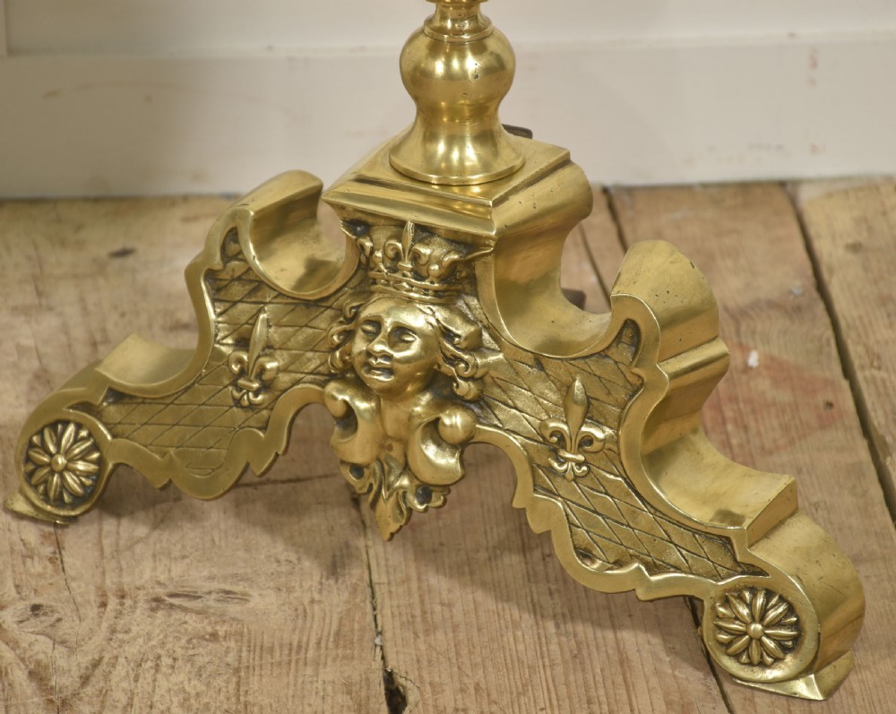 A pair of polished gilt brass andirons featuring double ball finials atop carved bases decorated with cherub faces, lattice work, and fleur-de-lis motifs. View VI