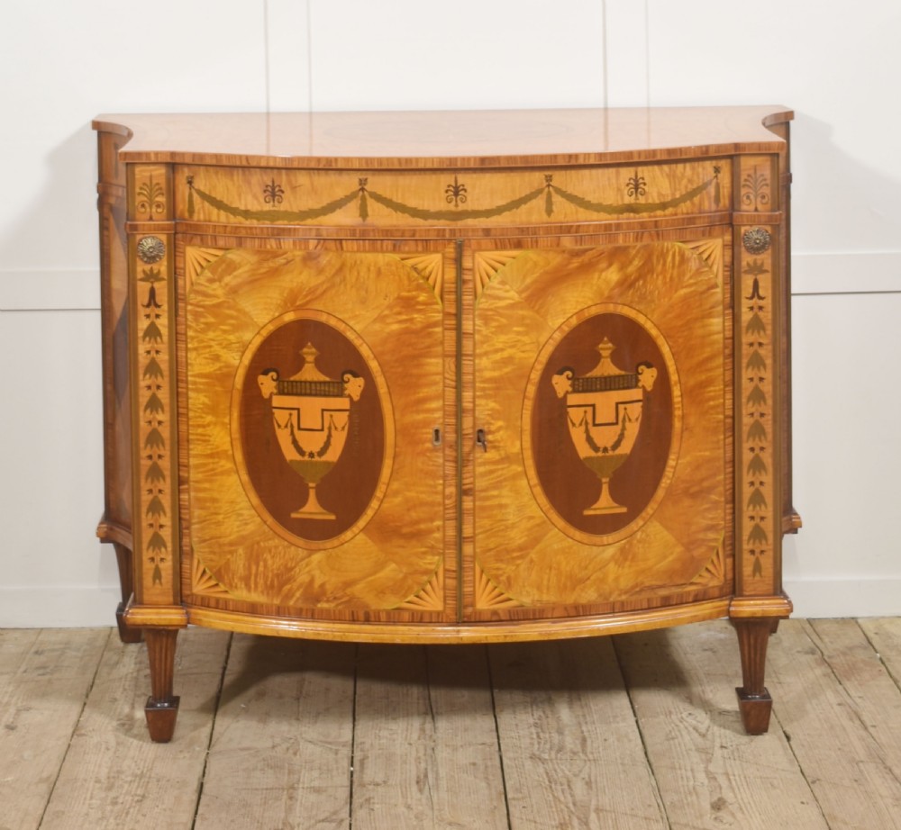 A Neoclassical demi-lune side cabinet crafted from golden satinwood featuring detailed urn marquetry inlays on two doors and tapered square legs.