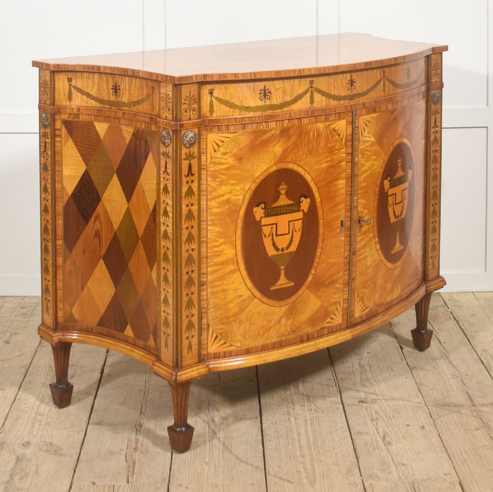 A Neoclassical demi-lune side cabinet crafted from golden satinwood featuring detailed urn marquetry inlays on two doors and tapered square legs. View IV