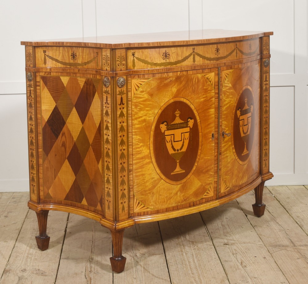 A Neoclassical demi-lune side cabinet crafted from golden satinwood featuring detailed urn marquetry inlays on two doors and tapered square legs. View V