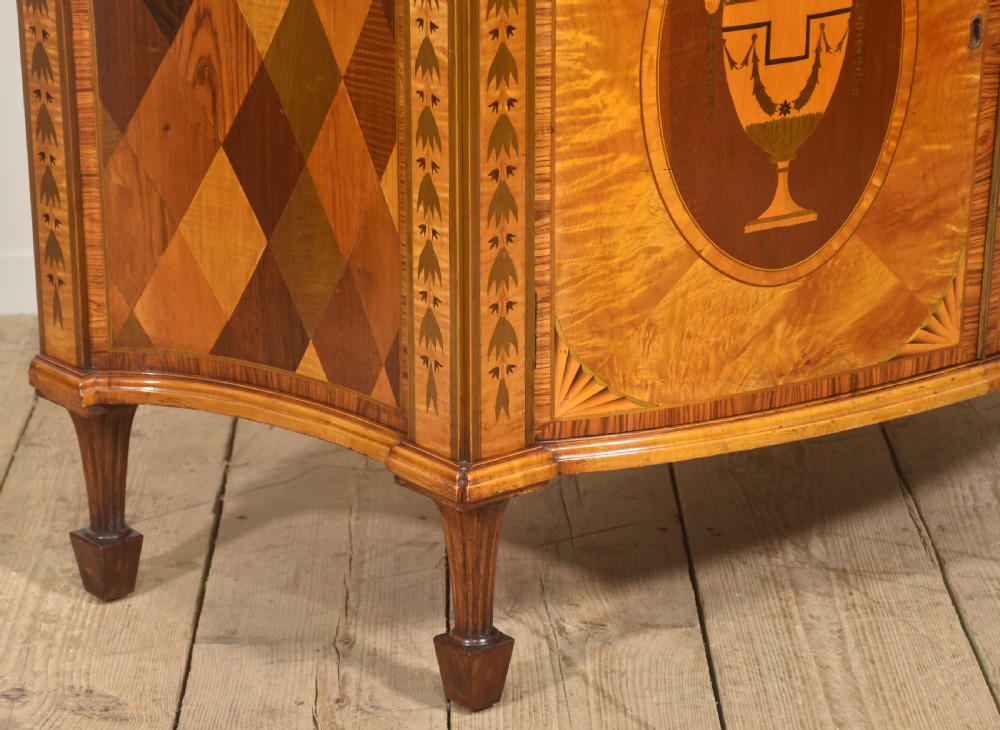 A Neoclassical demi-lune side cabinet crafted from golden satinwood featuring detailed urn marquetry inlays on two doors and tapered square legs. View VIII