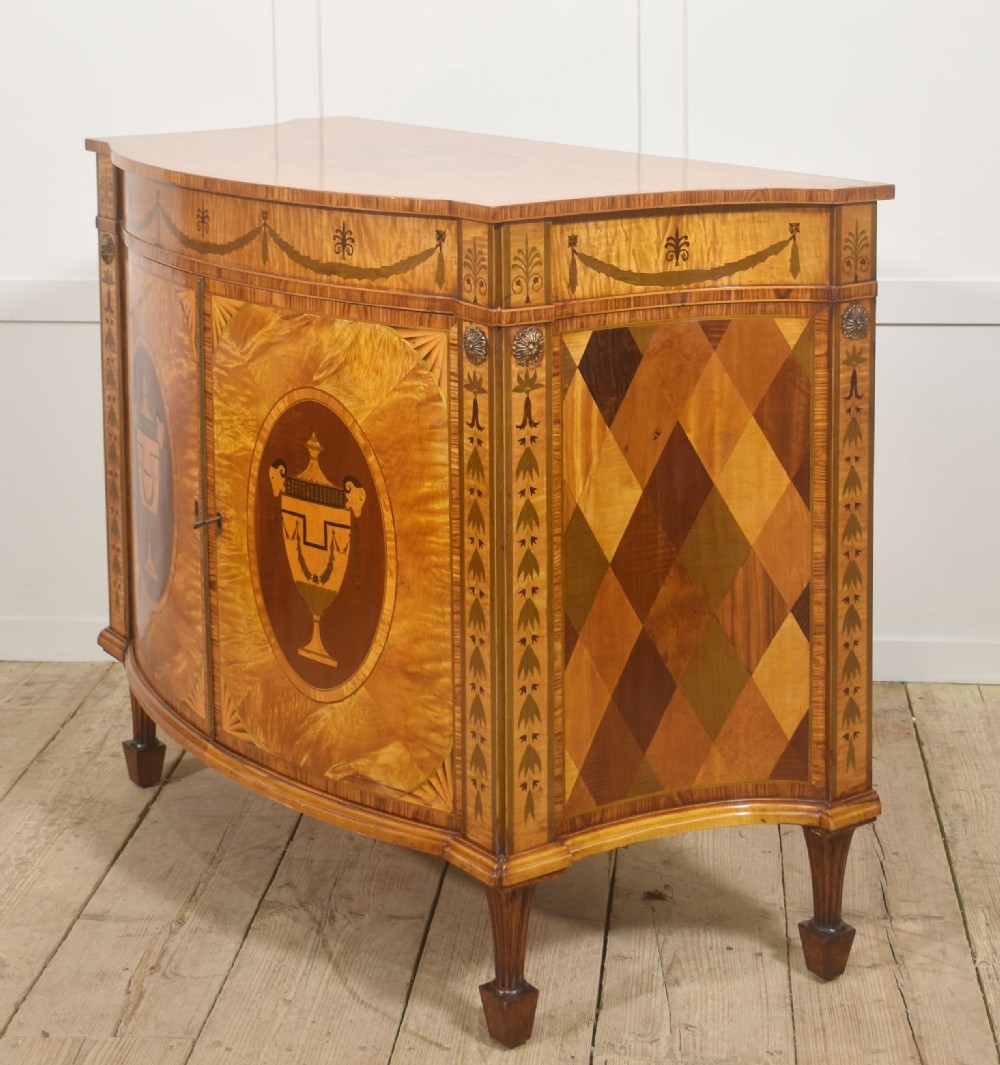 A Neoclassical demi-lune side cabinet crafted from golden satinwood featuring detailed urn marquetry inlays on two doors and tapered square legs. View X