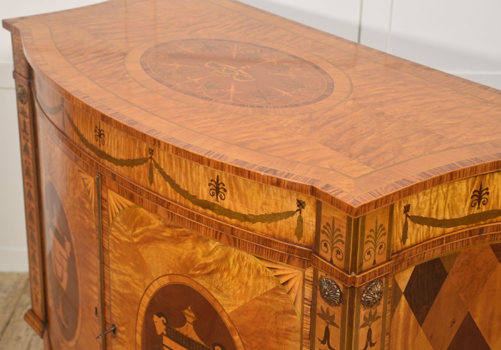 A Neoclassical demi-lune side cabinet crafted from golden satinwood featuring detailed urn marquetry inlays on two doors and tapered square legs. View XII