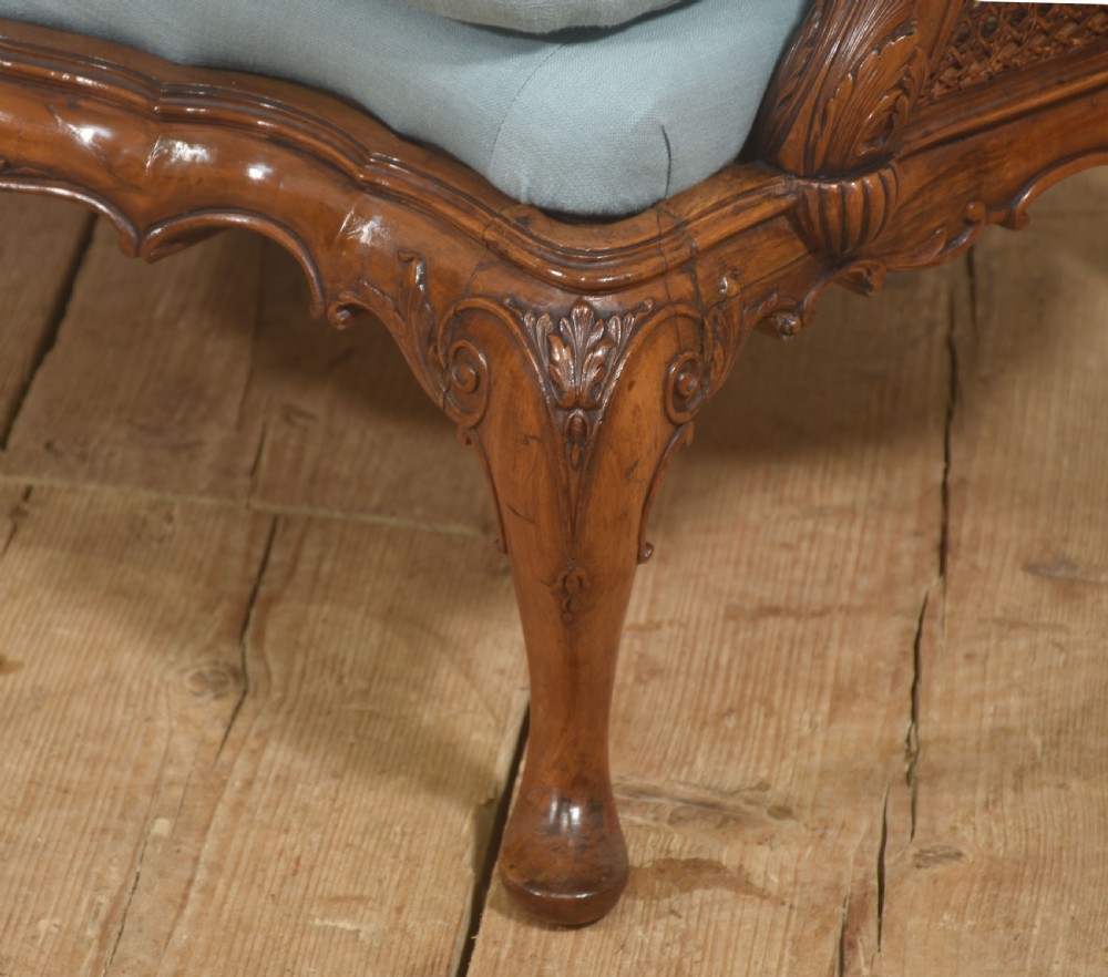 A Louis XV style carved walnut settee featuring a four-panel caned backrest, central burr walnut splats, light blue seat cushions, and carved cabriole legs. View V