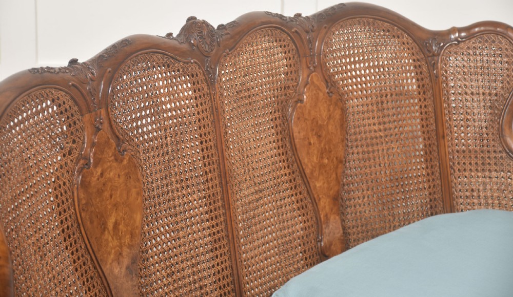 A Louis XV style carved walnut settee featuring a four-panel caned backrest, central burr walnut splats, light blue seat cushions, and carved cabriole legs. View VI