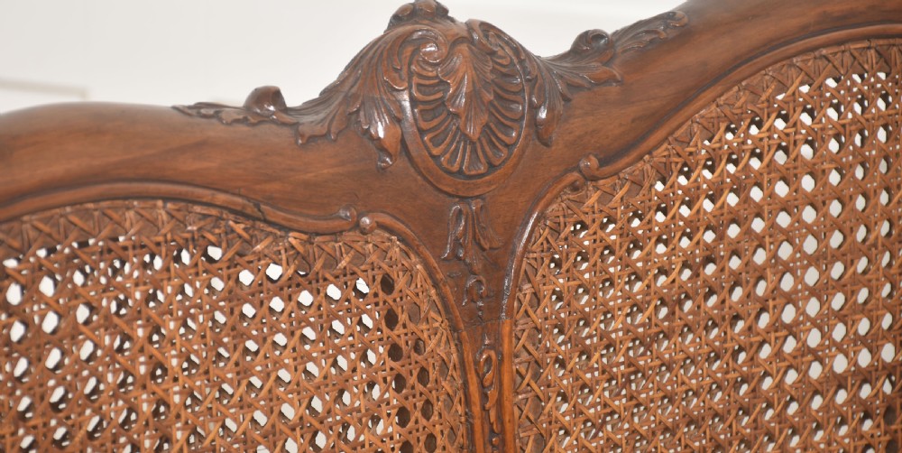 A Louis XV style carved walnut settee featuring a four-panel caned backrest, central burr walnut splats, light blue seat cushions, and carved cabriole legs. View VIII