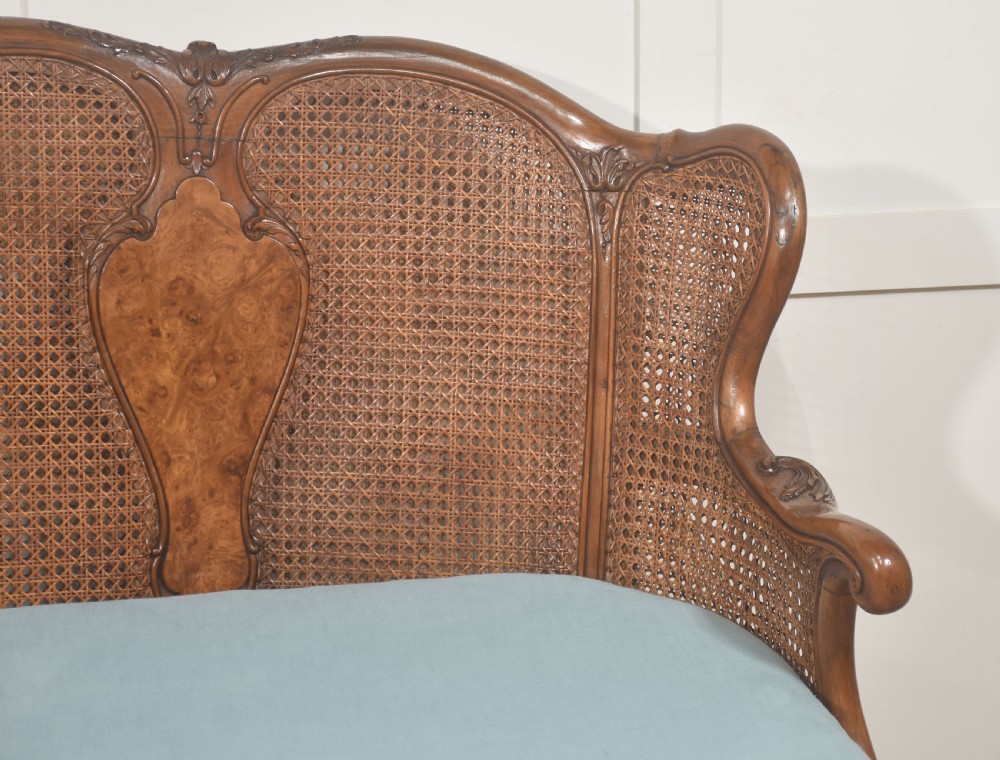 A Louis XV style carved walnut settee featuring a four-panel caned backrest, central burr walnut splats, light blue seat cushions, and carved cabriole legs. View XI