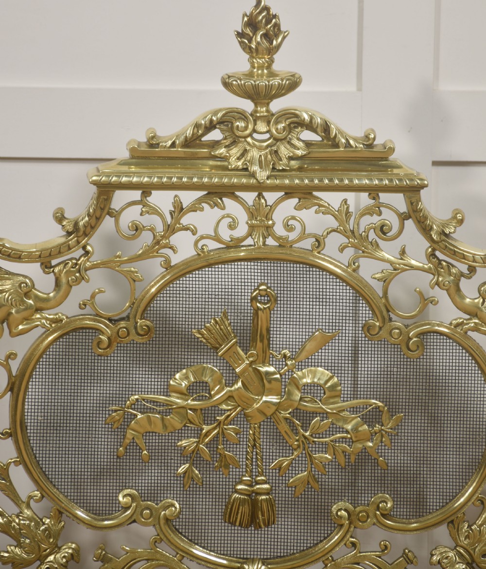 An ornate cast brass free-standing fire screen featuring pierced Rococo scrollwork, a mesh panel with torch and ribbon detailing, and scrolled feet. View III