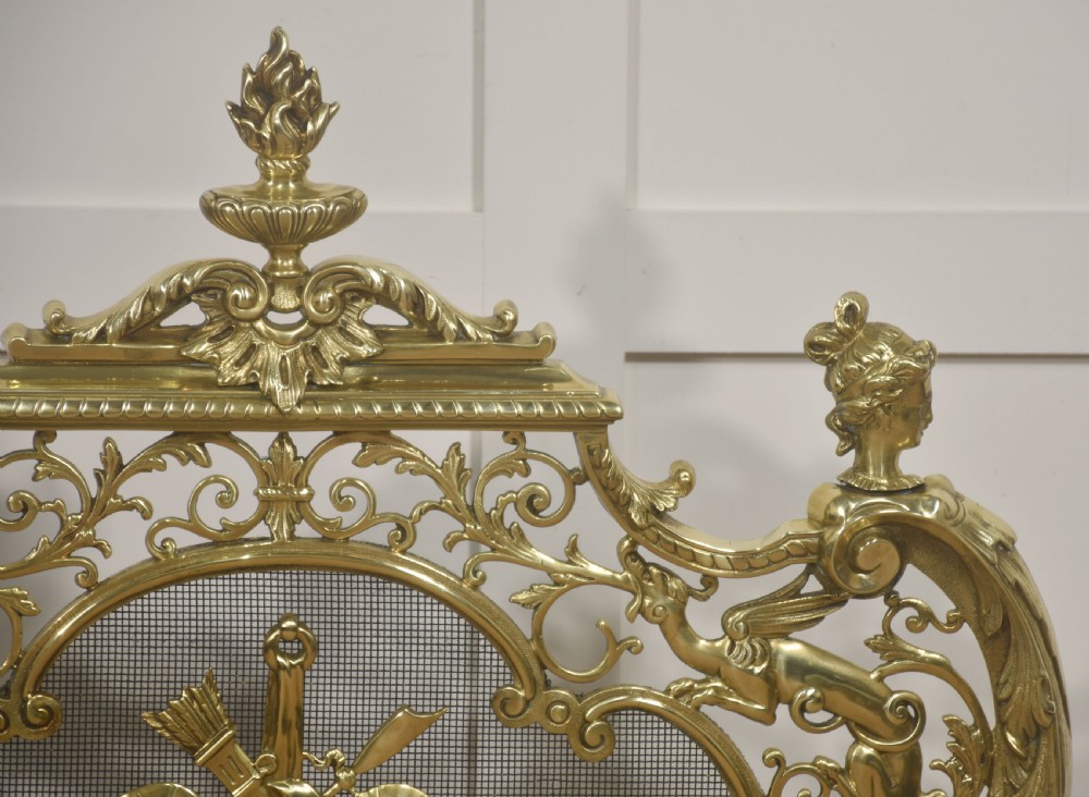 An ornate cast brass free-standing fire screen featuring pierced Rococo scrollwork, a mesh panel with torch and ribbon detailing, and scrolled feet. View V