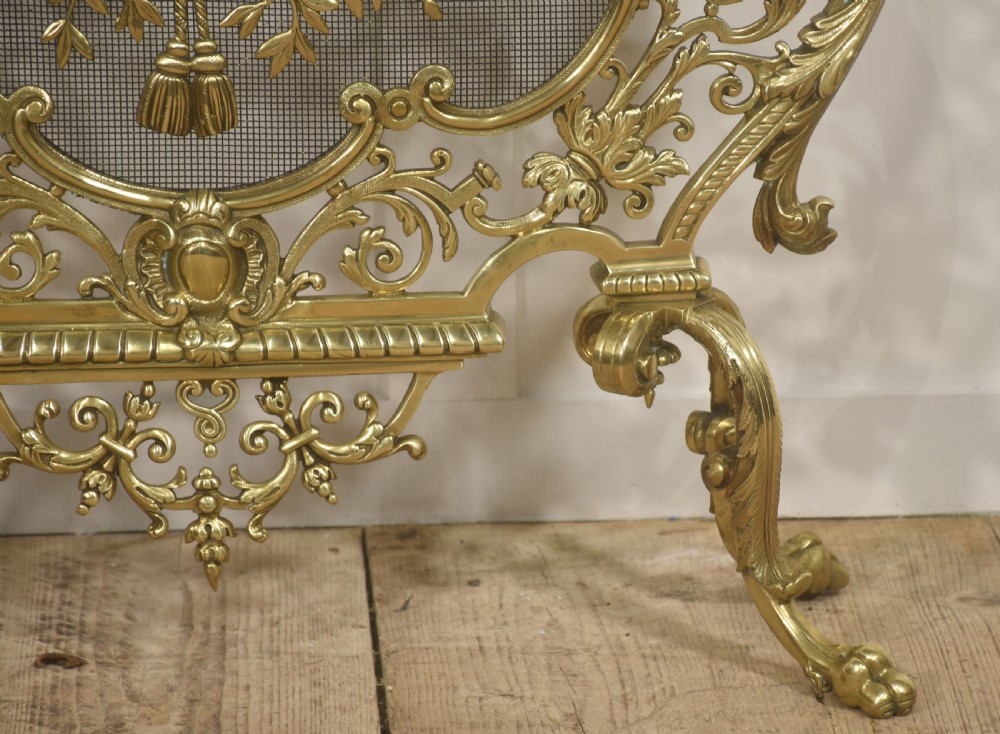 An ornate cast brass free-standing fire screen featuring pierced Rococo scrollwork, a mesh panel with torch and ribbon detailing, and scrolled feet. View VII