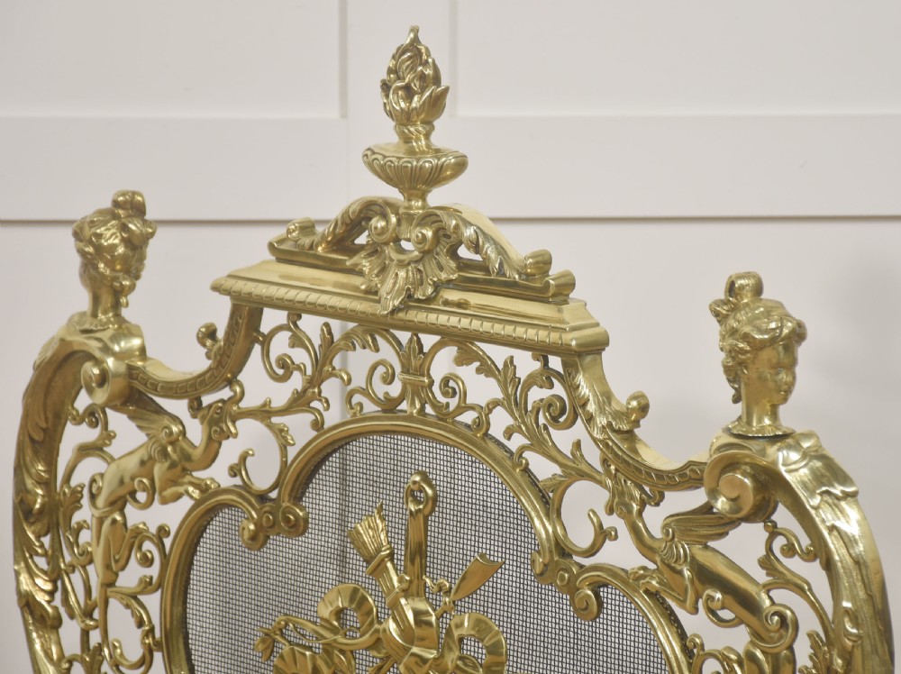 An ornate cast brass free-standing fire screen featuring pierced Rococo scrollwork, a mesh panel with torch and ribbon detailing, and scrolled feet. View VIII