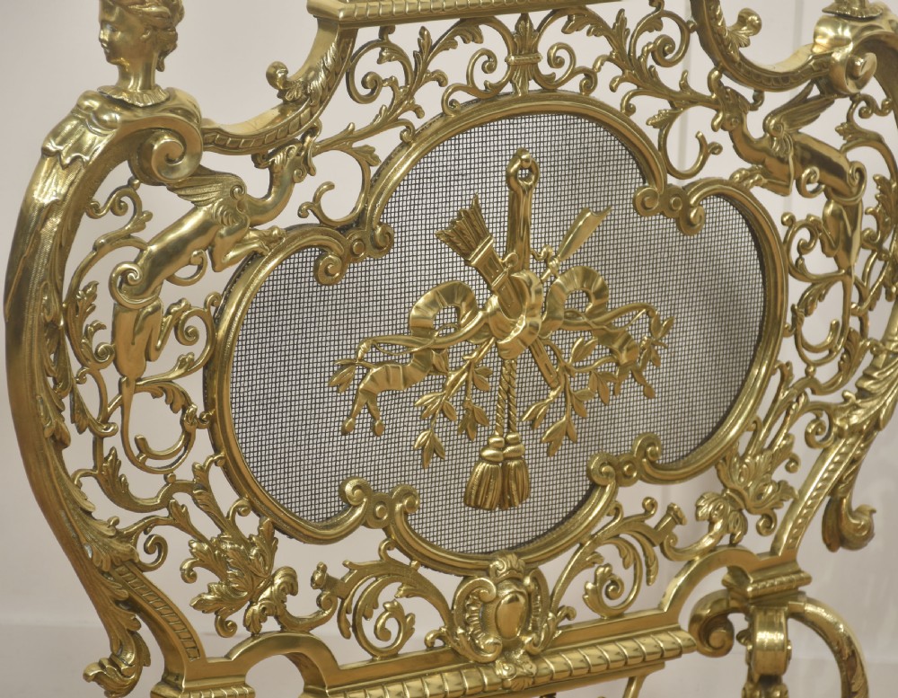 An ornate cast brass free-standing fire screen featuring pierced Rococo scrollwork, a mesh panel with torch and ribbon detailing, and scrolled feet. View X