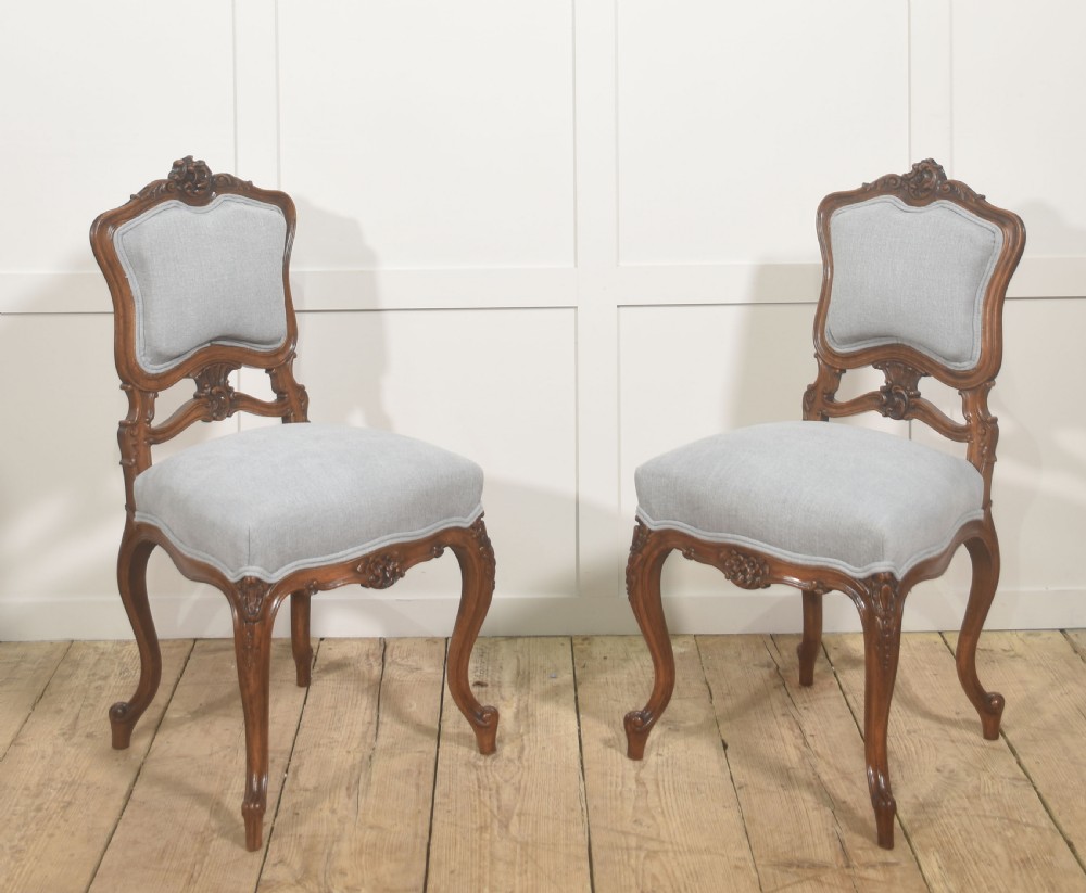 A pair of carved walnut Louis XV style side chairs with light grey upholstery on the seats and padded backrests.