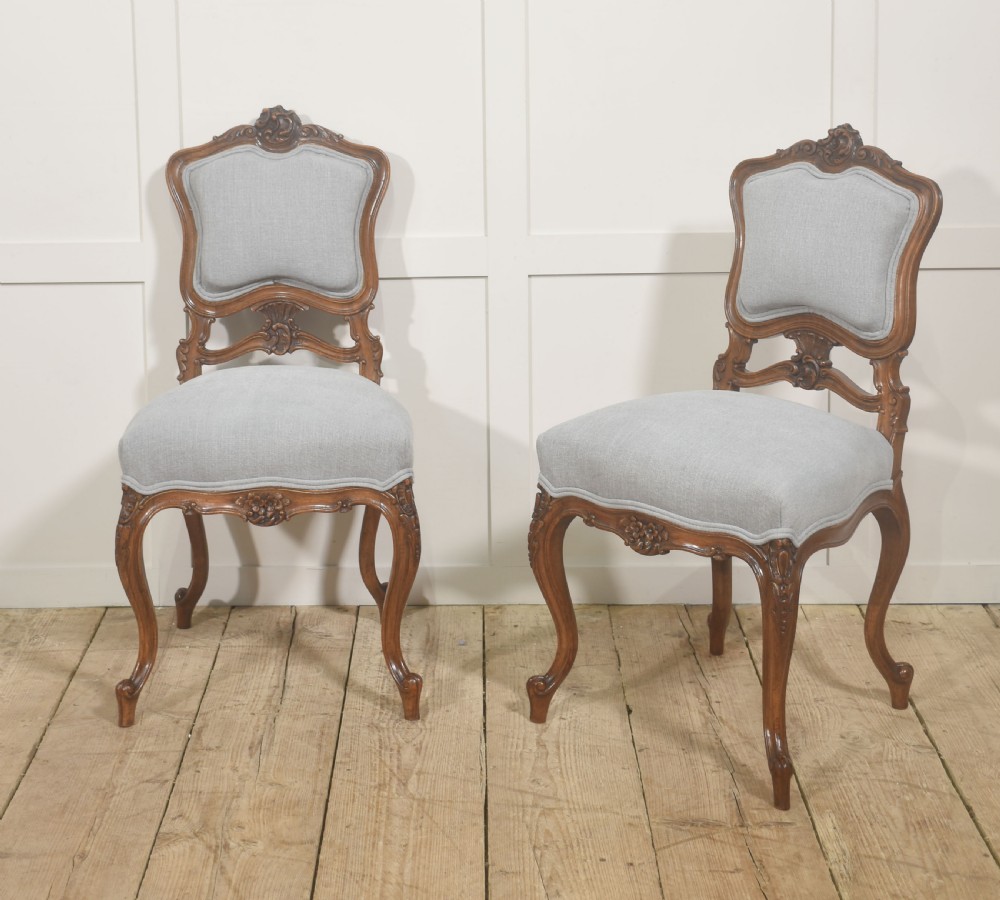 A pair of carved walnut Louis XV style side chairs with light grey upholstery on the seats and padded backrests. View VI