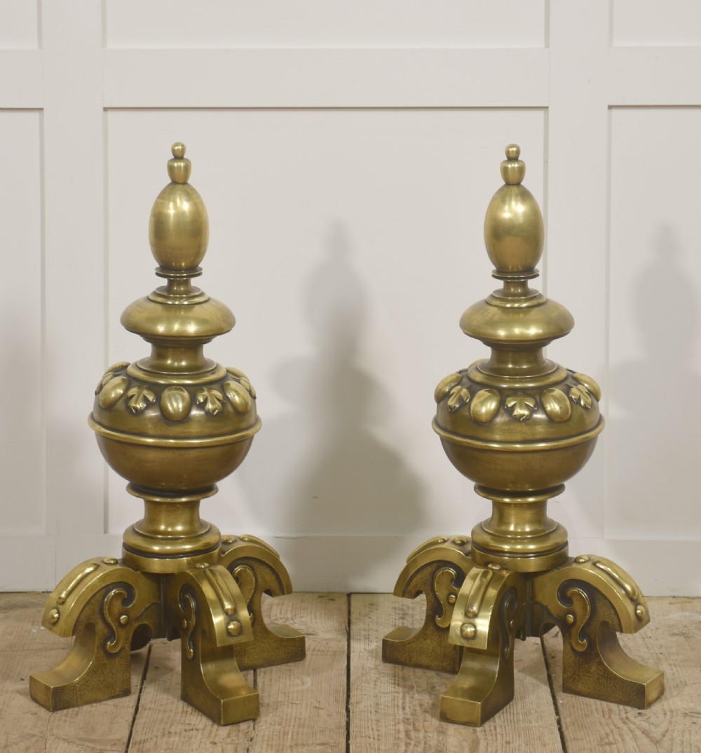 A pair of substantial cast brass fire dogs featuring urn-shaped finials, gadrooned central spheres, and ornate scroll feet.