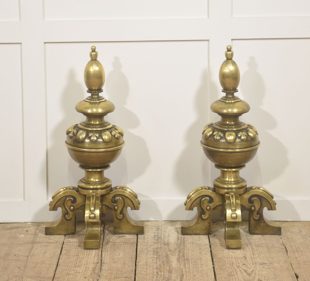 A pair of substantial cast brass fire dogs featuring urn-shaped finials, gadrooned central spheres, and ornate scroll feet. View V