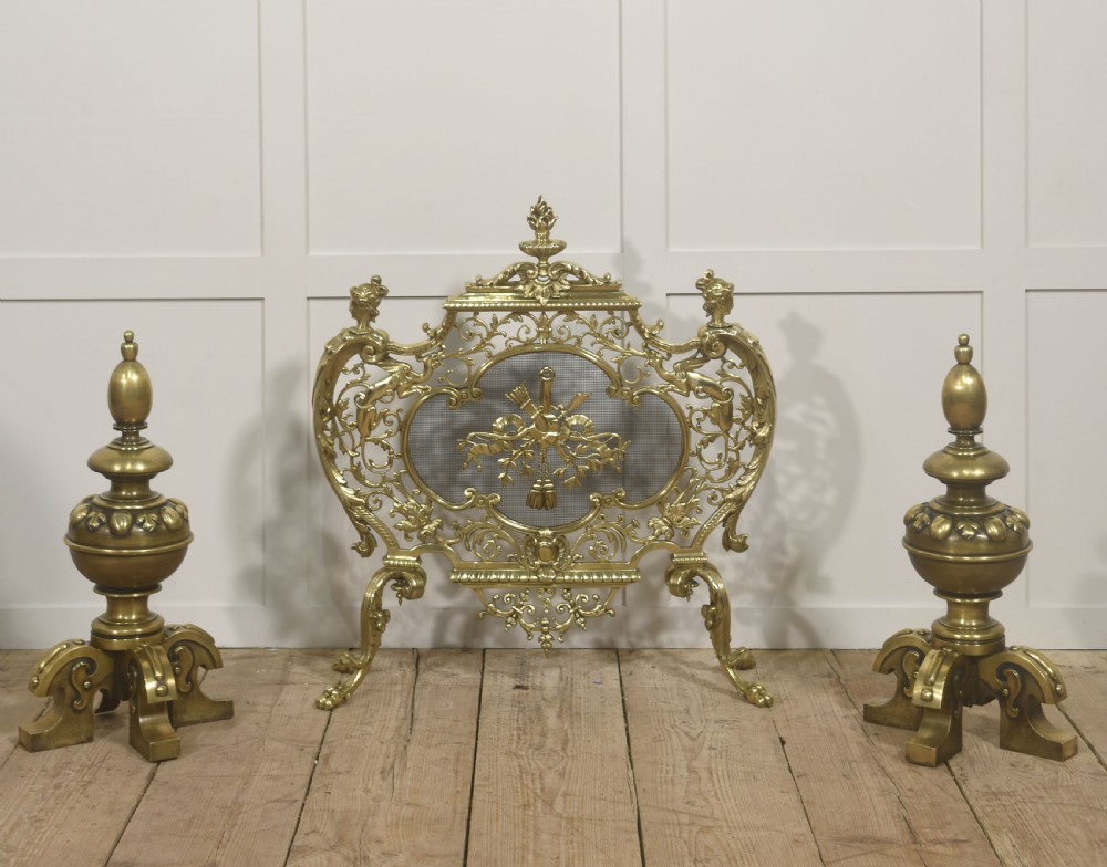 A pair of substantial cast brass fire dogs featuring urn-shaped finials, gadrooned central spheres, and ornate scroll feet. View VI