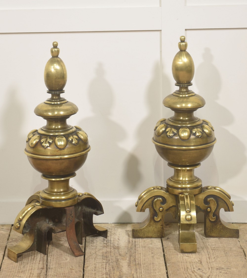 A pair of substantial cast brass fire dogs featuring urn-shaped finials, gadrooned central spheres, and ornate scroll feet. View VII
