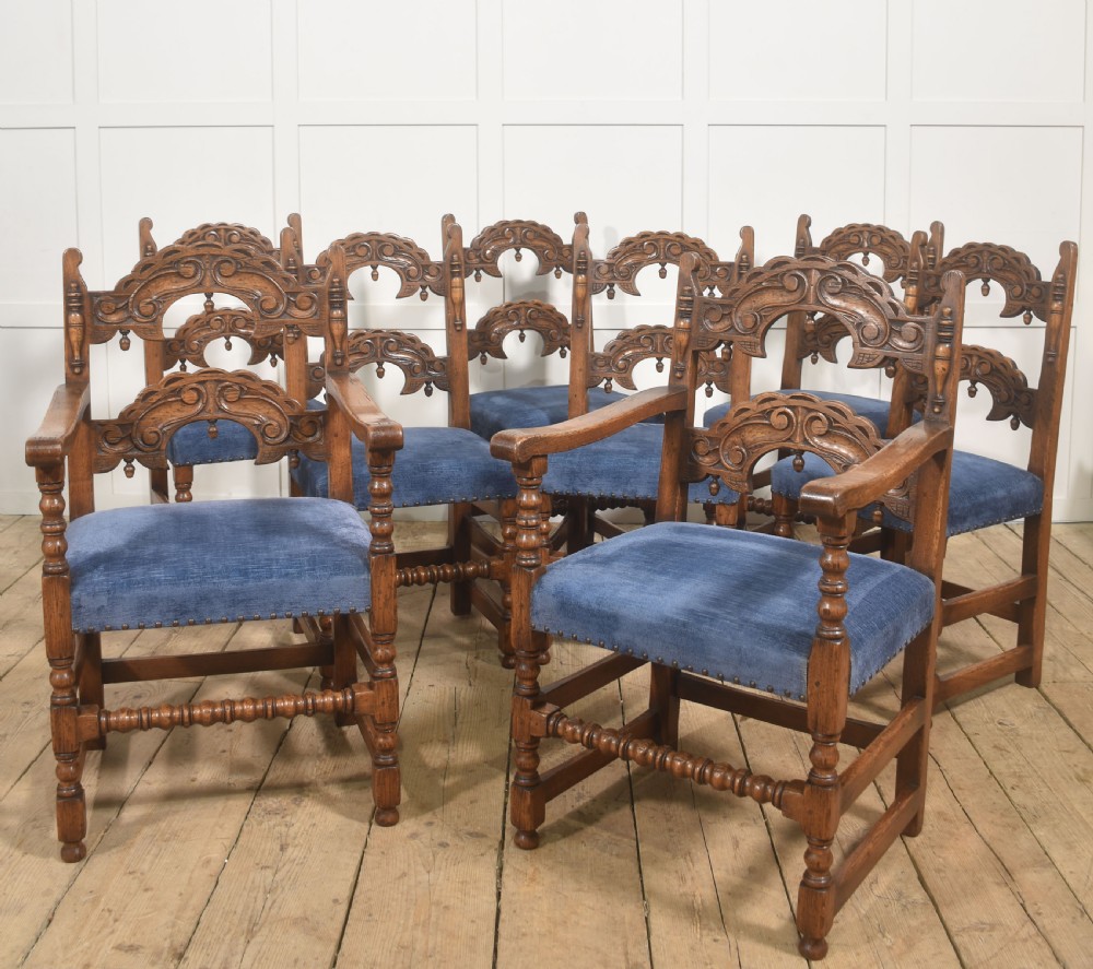 A set of eight Jacobean Revival carved oak dining chairs with blue velvet upholstered seats, including two carver armchairs and six side chairs.
