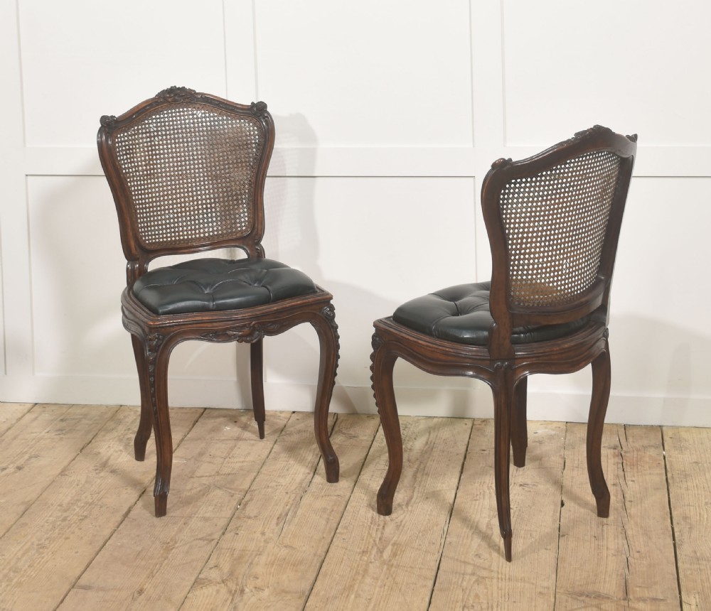A pair of carved walnut side chairs in the Louis XV style, featuring woven cane backs, dark leather button-tufted seats, and cabriole legs. View II